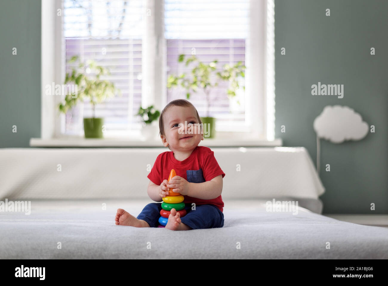 Glückliches Kind mit farbigen Pyramide Spielzeug auf weißen Bett in seinem Zimmer Stockfoto