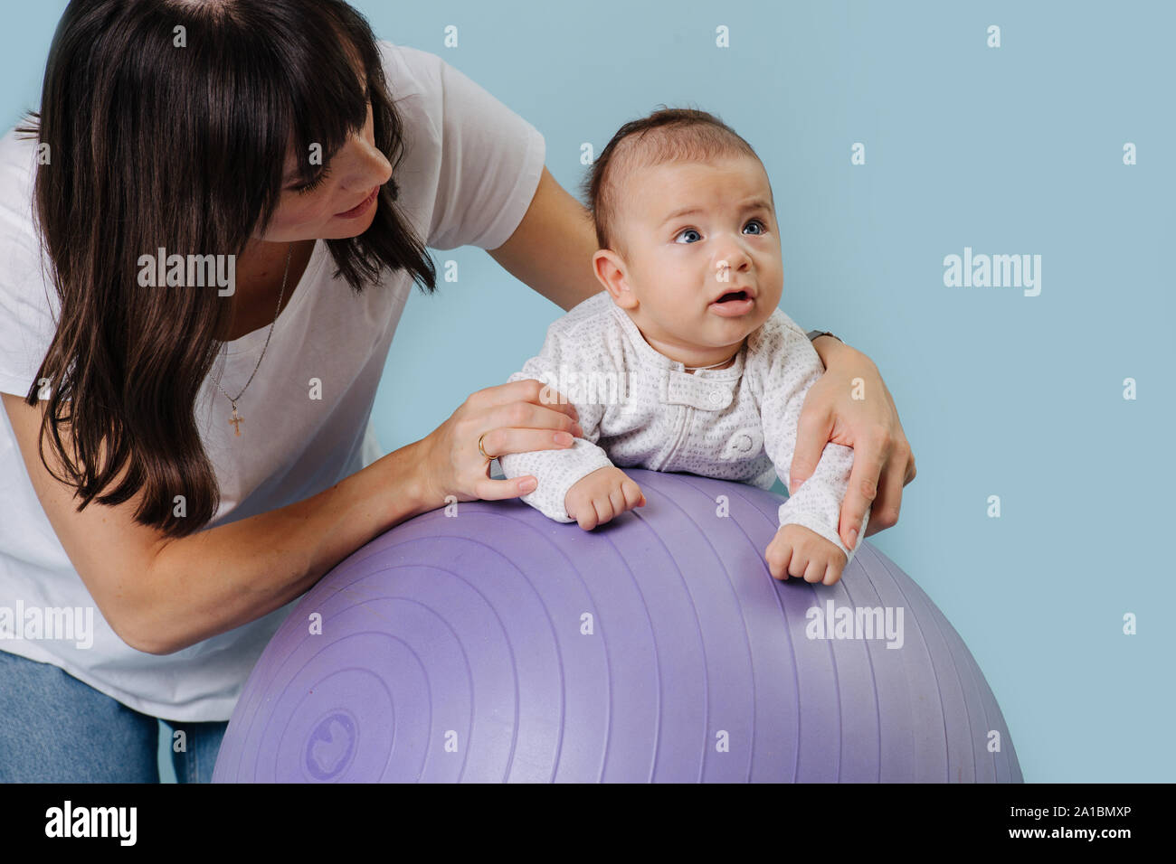 Glückliche Mutter Übungen mit Ihrem Kleinkind Baby auf lila Yoga ball Stockfoto