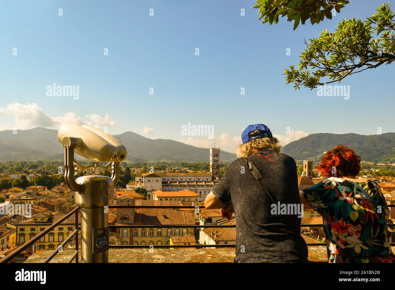 Panoramablick auf die Innenstadt von Lucca vom Torre Guinigi Turm mit ein paar Touristen von hinten und ein Fernglas im Sommer, Toskana, Italien Stockfoto