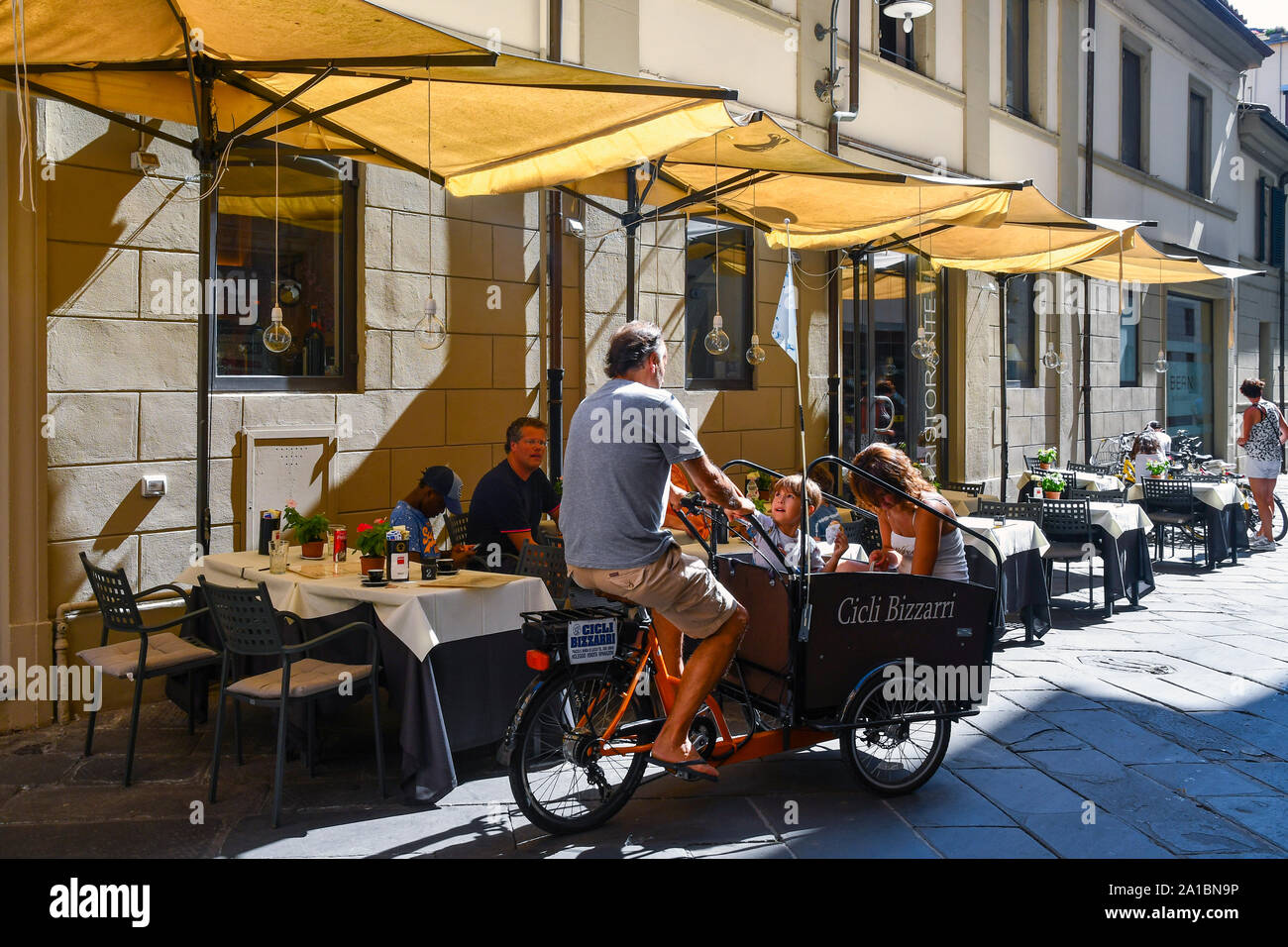 Blick auf die Straße im historischen Zentrum von Lucca mit einem Vater, sein Sohn und seine Frau auf einem cargo Fahrrad vor ein Restaurant im Freien, Toskana, Italien Stockfoto