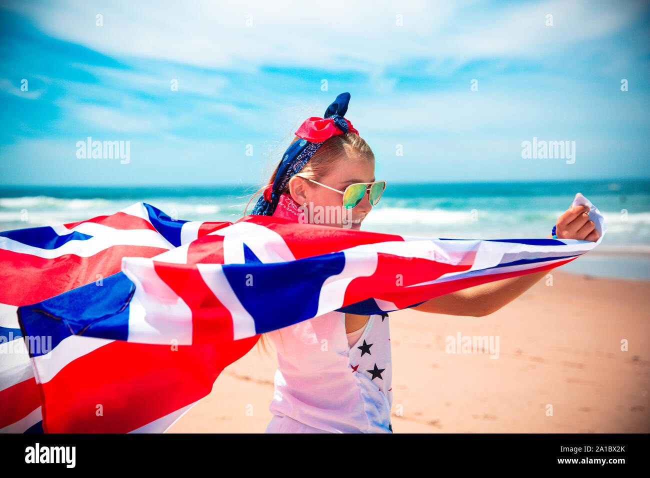 Gerne britische Mädchen trägt flattern Blau Weiß Rot Flagge von Großbritannien, des Vereinigten Königreichs und Nordirland gegen den blauen Himmel und das Meer zurück Stockfoto