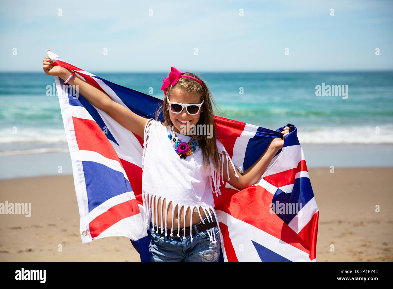 Gerne britische Mädchen trägt flattern Blau Weiß Rot Flagge von Großbritannien, des Vereinigten Königreichs und Nordirland gegen den blauen Himmel und das Meer zurück Stockfoto