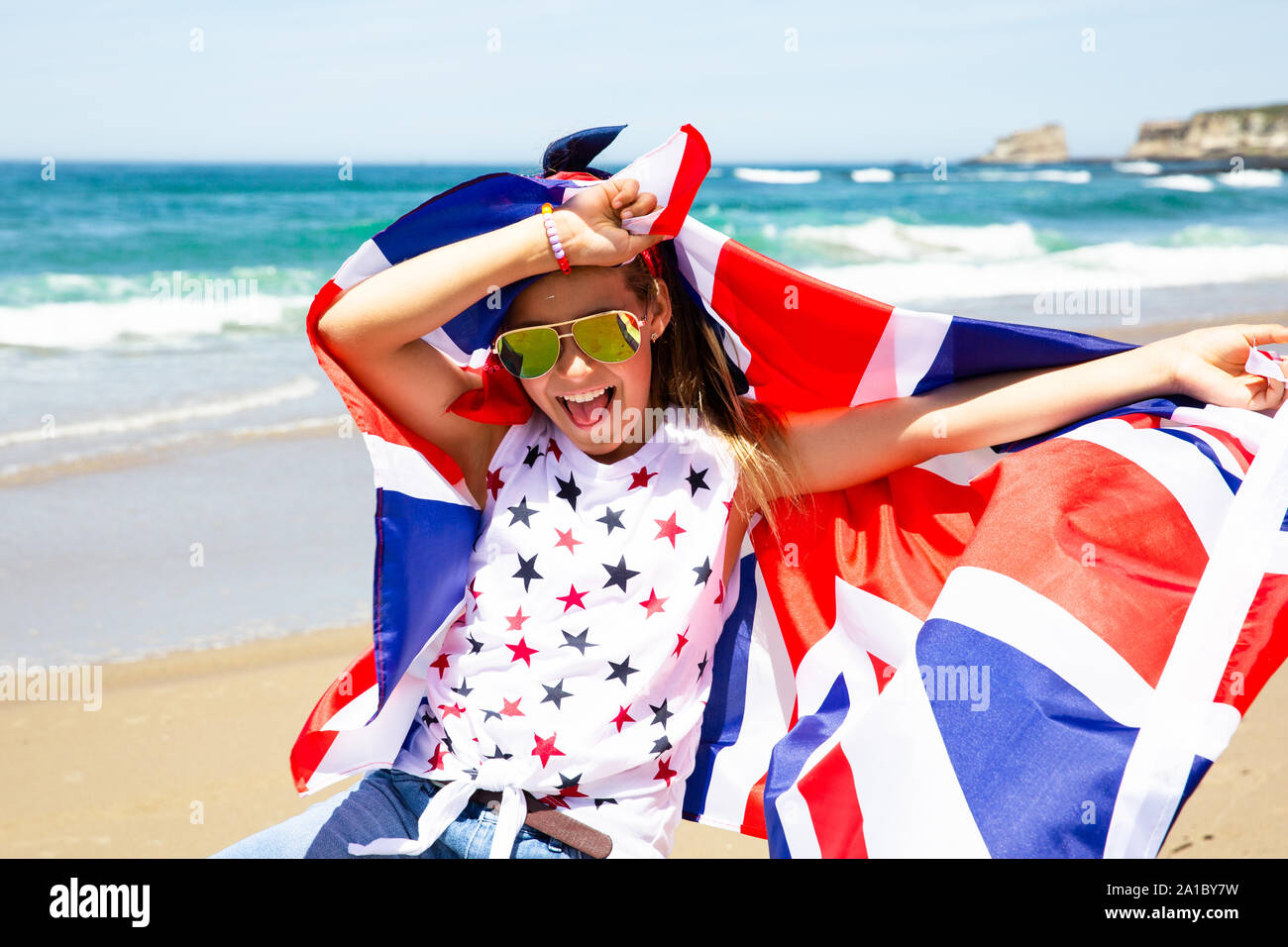 Gerne britische Mädchen trägt flattern Blau Weiß Rot Flagge von Großbritannien, des Vereinigten Königreichs und Nordirland gegen den blauen Himmel und das Meer zurück Stockfoto