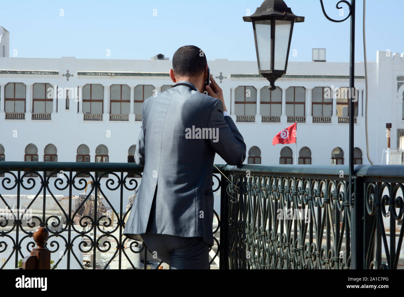Eine junge tunesische Geschäftsmann in Anzug nimmt einen geschäftlichen Anruf auf seinem Handy auf einer Terrasse mit Blick auf die Medina von Tunis, Tunesien. Stockfoto