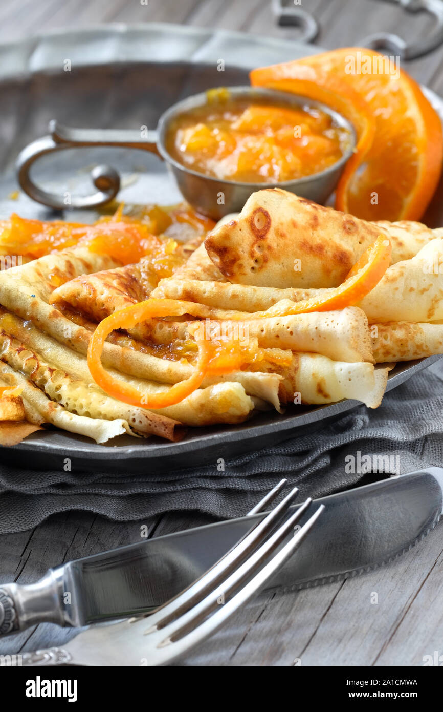 Crepes Suzette auf vintage Metallplatte auf Holztisch mit orange Sauce serviert, vertikale Nahaufnahme Stockfoto