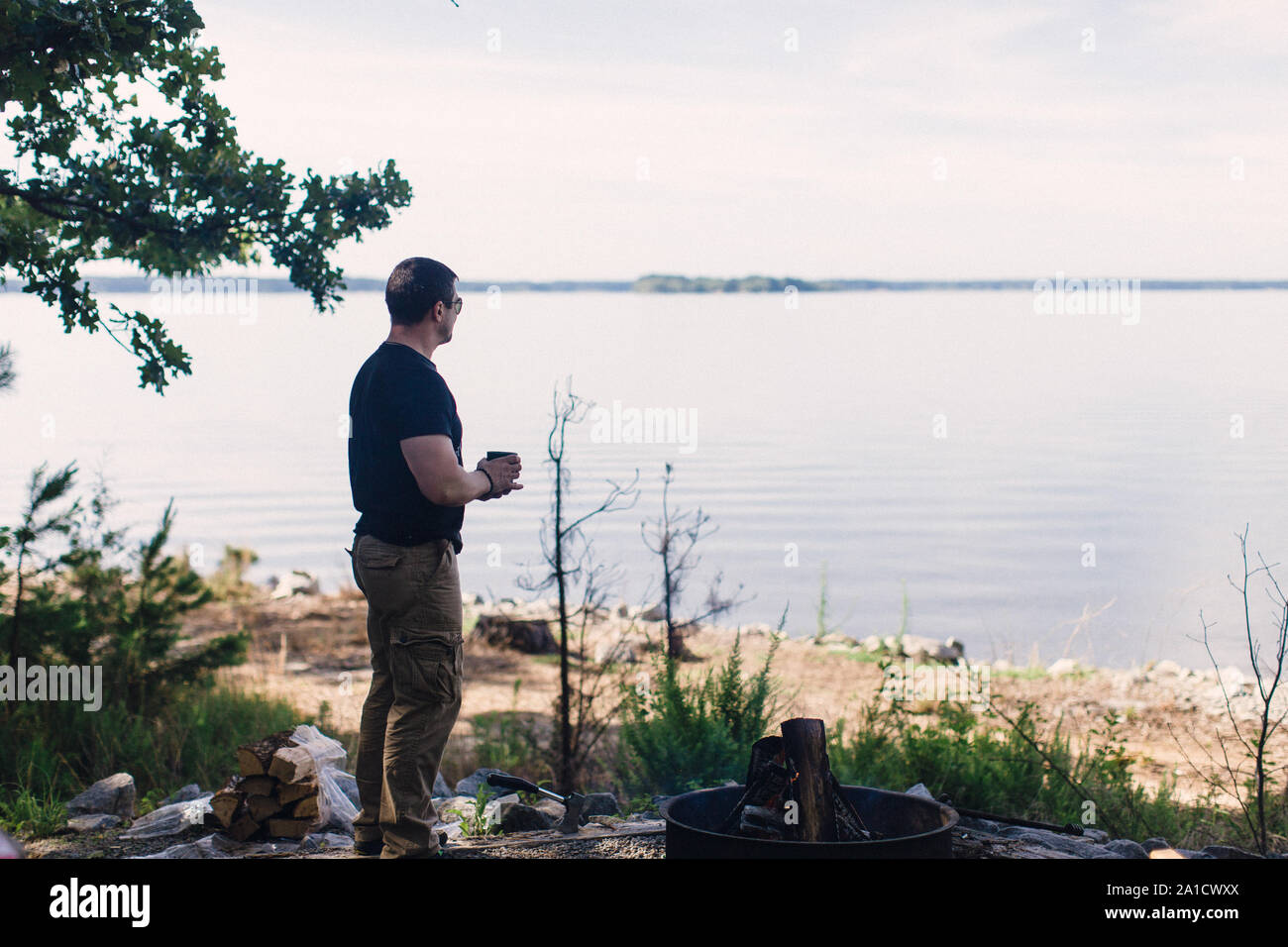 Mitte Alter kaukasischer Mann steht an der campside durch den See bei einer Tasse Kaffee Stockfoto