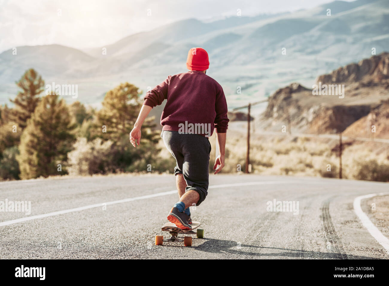 Mann Hipster ist Skateboarding bei Mountain Road im Abendlicht Stockfoto