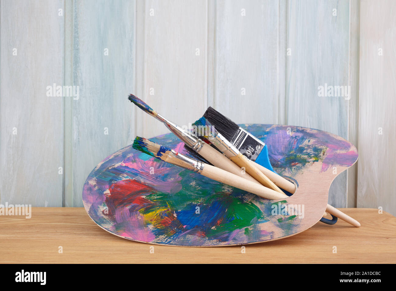Holz Palette mit Farben und Pinsel auf farbigen Holz- Hintergrund Stockfoto