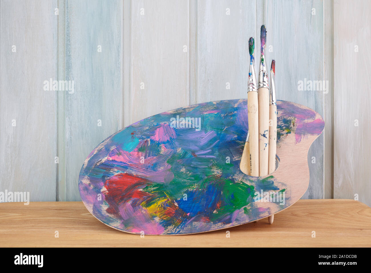 Holz Palette mit Farben und Pinsel auf farbigen Holz- Hintergrund Stockfoto