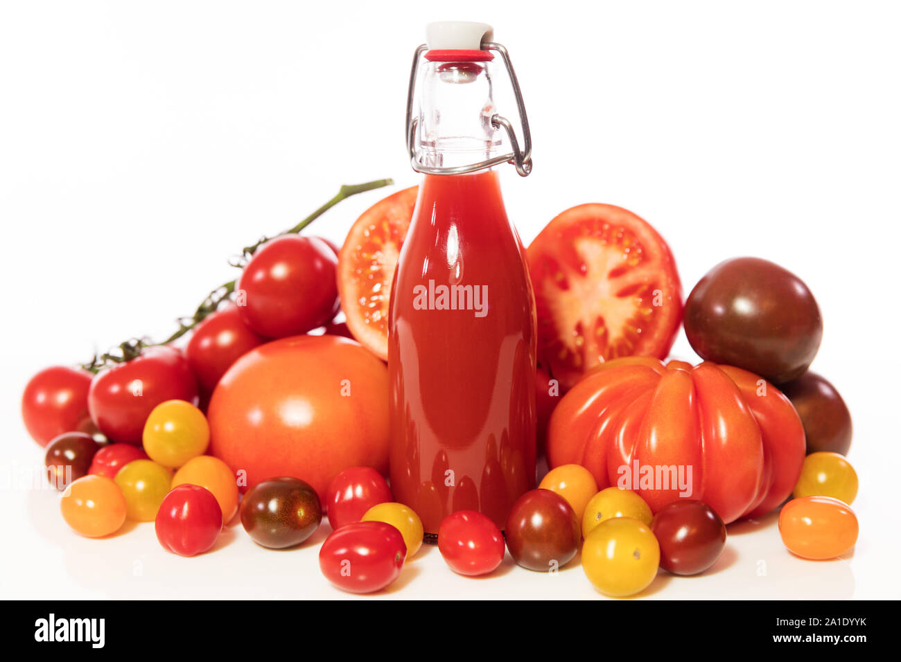 Eine Menge von verschiedenen Tomaten und eine volle Flasche mit Saft oder Tomatensoße, vor weißen Stockfoto