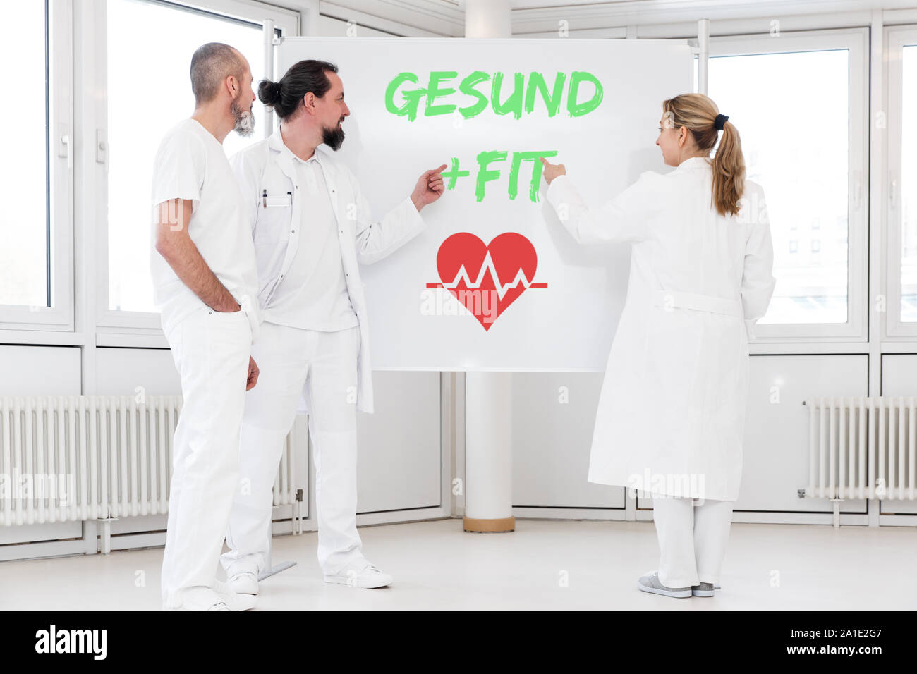 Medizin Personal steht vor einer Tafel, auf der die deutschen Wörter gesund und fit Das bedeutet gesund. Ein rotes heartsymbol unter ihnen. c Stockfoto
