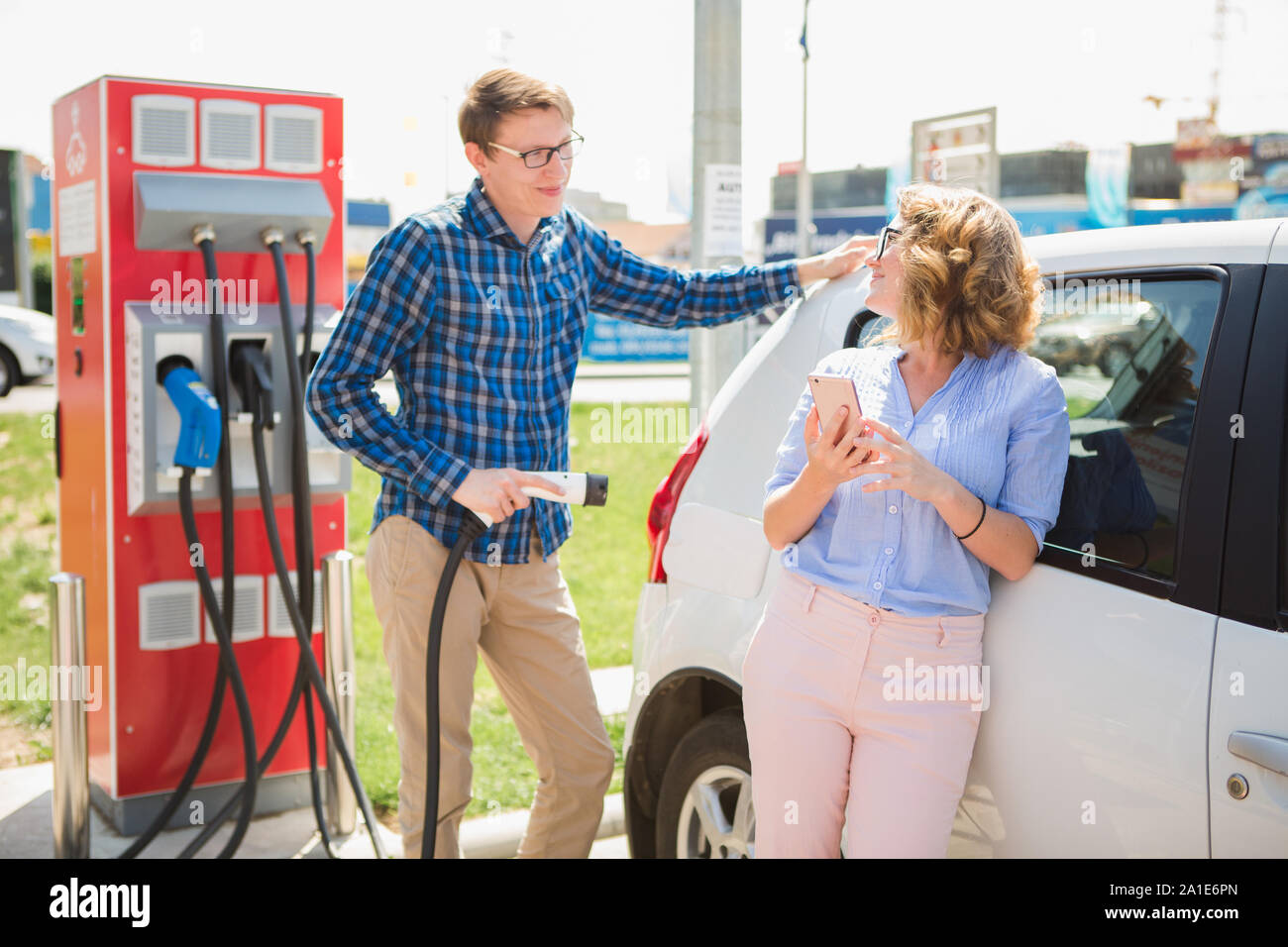 Mann und Frau stehen in der Nähe des Elektroautos. Das Auto wird der Ladevorgang an der Ladestation für Elektrofahrzeuge. Stockfoto