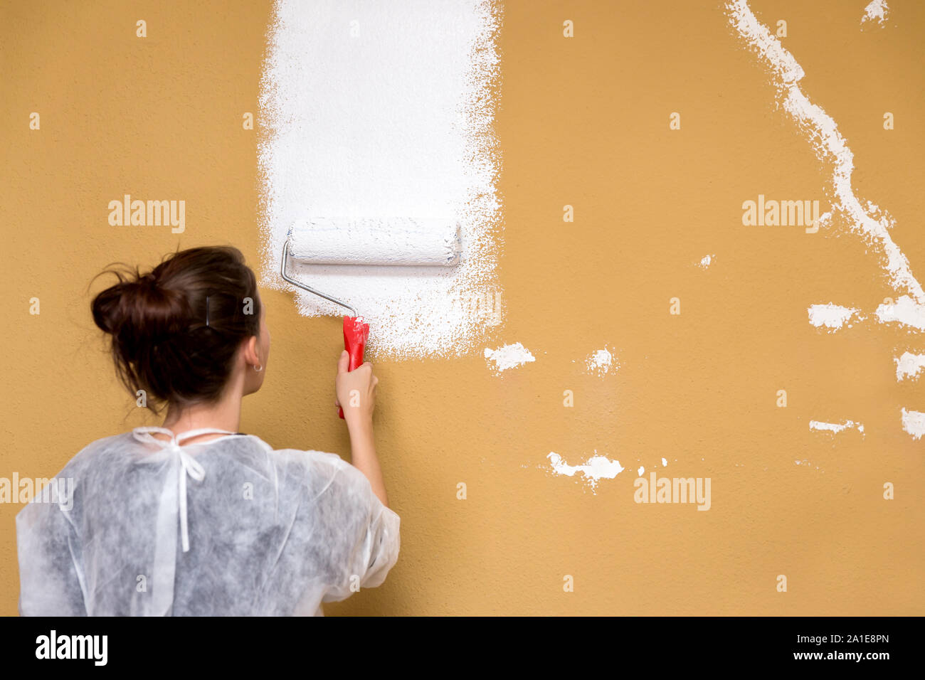 Junge Frau Malerei einen braunen Wand in der Farbe weiß, die Renovierung und die Verbesserung Stockfoto