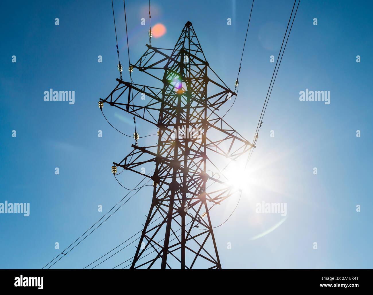 Metall Strommast mit Glas Isolatoren, Drähte und helle Sonne mit Highlights auf dem Hintergrund der klare, blaue Himmel Stockfoto