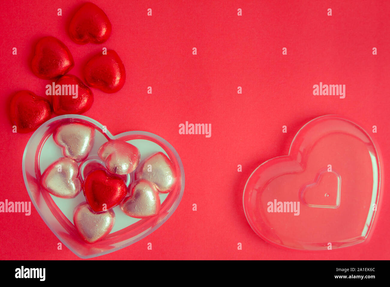 Blick von oben auf die Herzförmigen Bonbons in einer Box auf einem roten Hintergrund. Rotes Herz in einem Glas auf einem roten Hintergrund am Valentinstag. Roter Hintergrund mit Hea Stockfoto