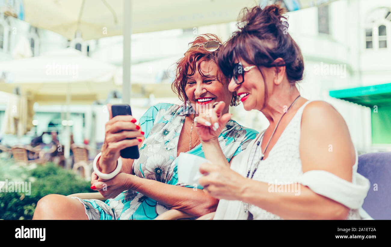 Zwei glückliche älterer Frauen Freunde über ein Smart Phone und sprechen beim Sitzen draußen in einem Café Stockfoto