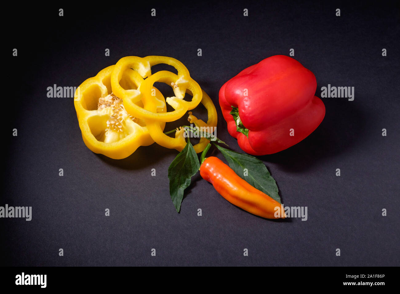 Gelbe Paprika in Scheiben geschnitten mit ganzen Red Paprika und eine rote Banane Pfeffer auf dunklem Hintergrund Stockfoto
