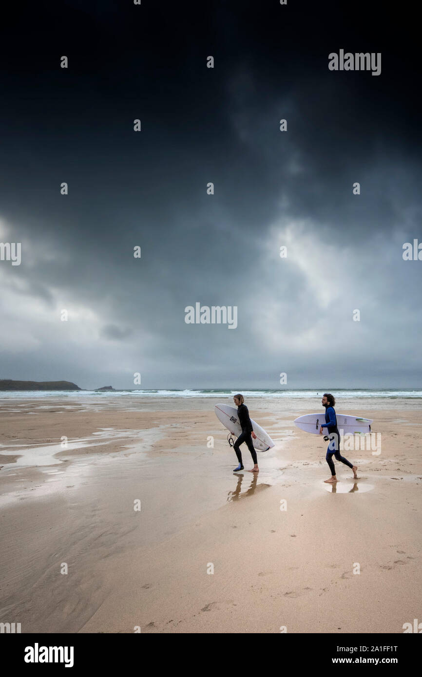 Surfer gehen auf den Fistral Beach als dunkle, düstere Gewitterwolken in Newquay in Cornwall. Stockfoto