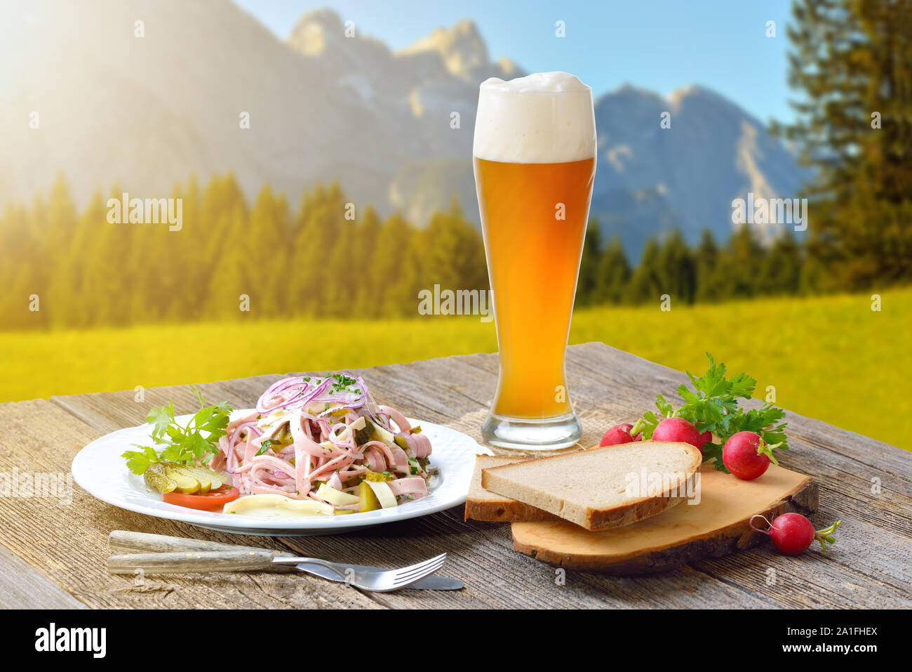 Herzhafte bayerische Wurstsalat mit Käse und Rustikales Brot mit einem Weißbier serviert, im Hintergrund die Berge von Zugspitze-Group Stockfoto