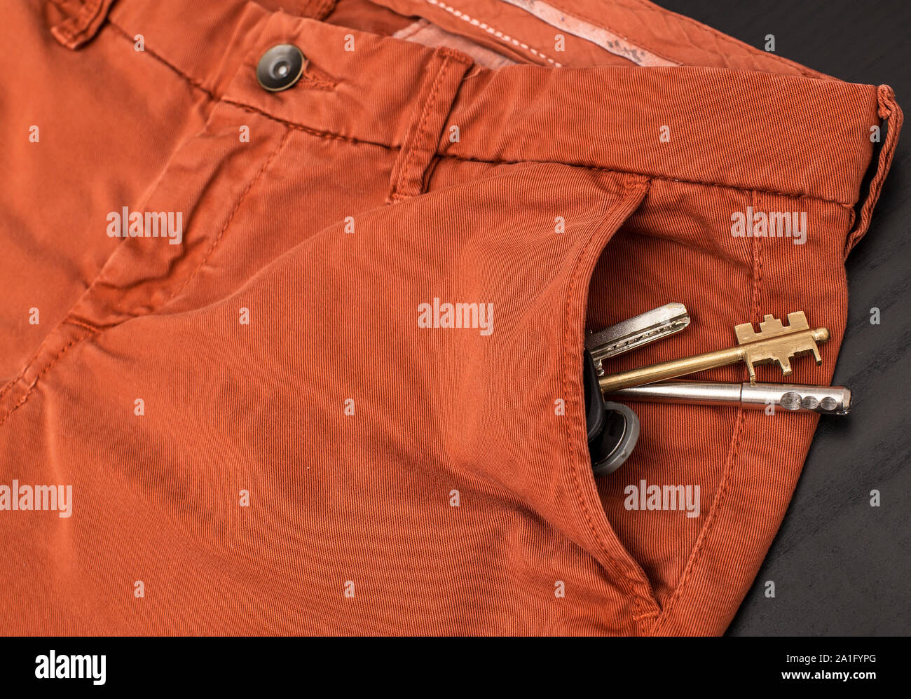 Ein Bündel von Schlüsseln ist in die Tasche rot Hose, die auf dem schwarzen Schreibtisch liegen Stockfoto