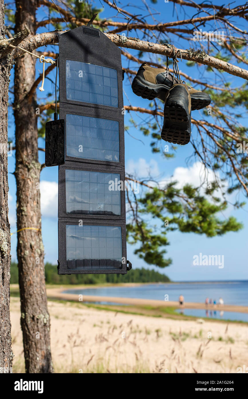 Tragbare solar panel auf einer Pinie, und lädt das Handy im Feld Bedingungen vor dem Hintergrund der Strand mit Leuten, Nea hängen Stockfoto