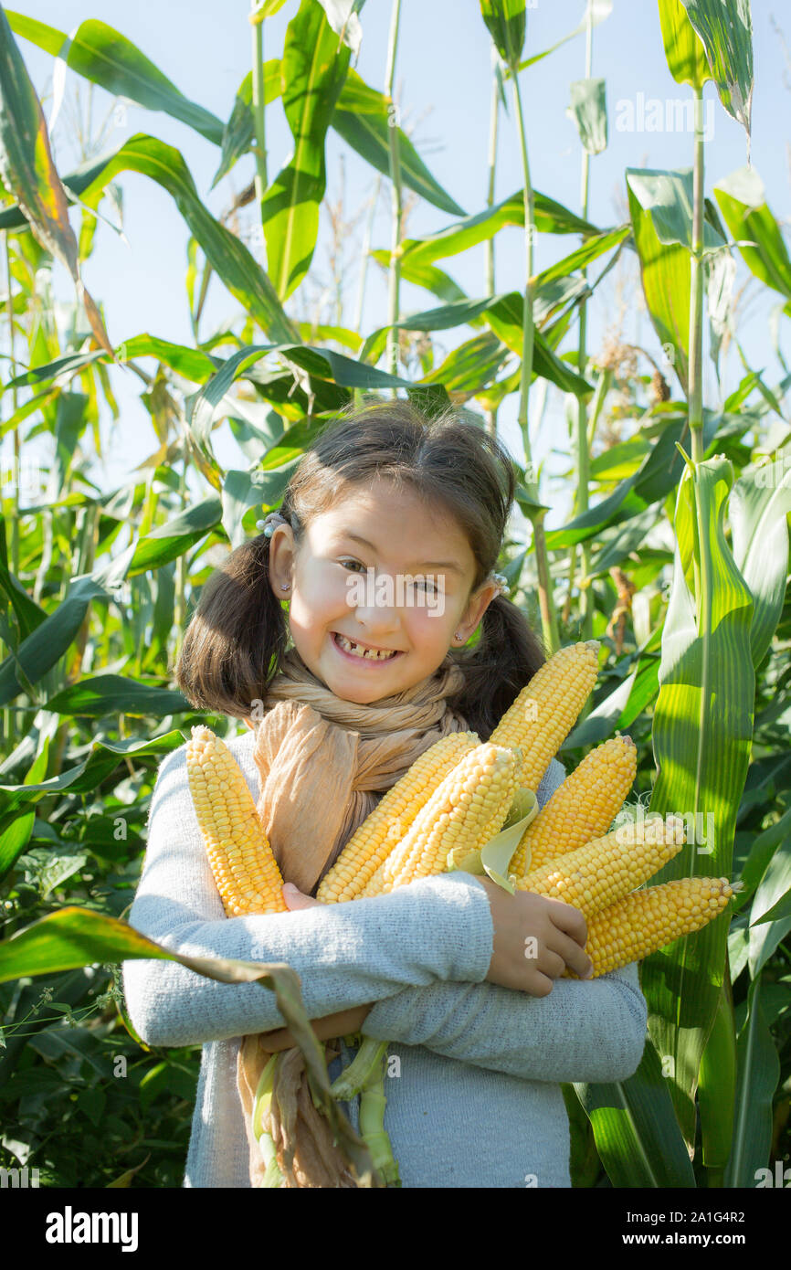 Happy kleines Mädchen hält Ähren. Froh, dass weibliches Kind in legere Kleidung outdoor. Lächelnd Kind im Dorf. Mädchen mit zufriedenen Gesichtsausdruck. Posi Stockfoto