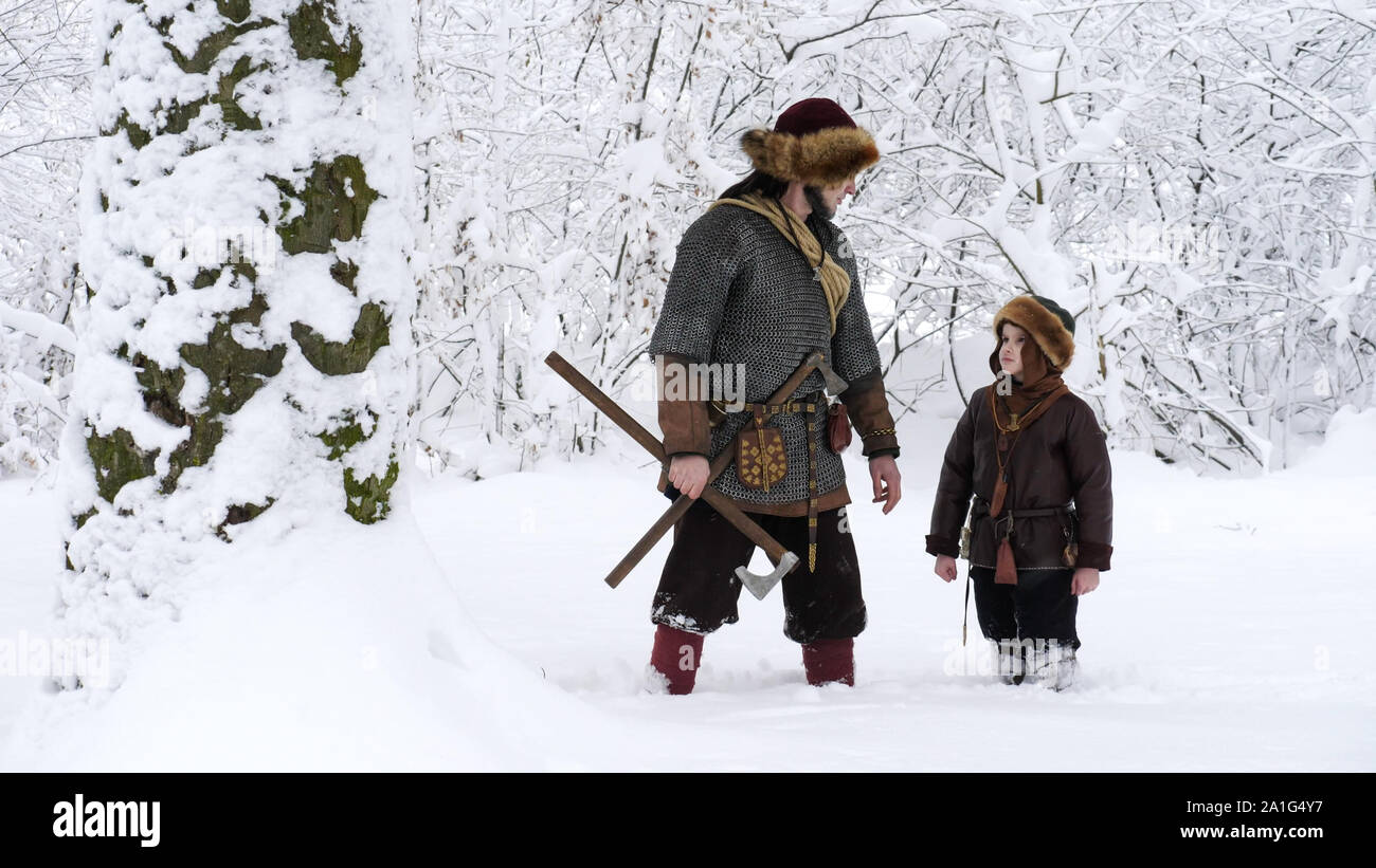 Vater Viking mit Seinem Sohn im Winter Wald. Vater geht mit seinem Sohn, der Besitz in den Händen ax. Sie gekleidet in mittelalterlichen Kleidern. Stockfoto