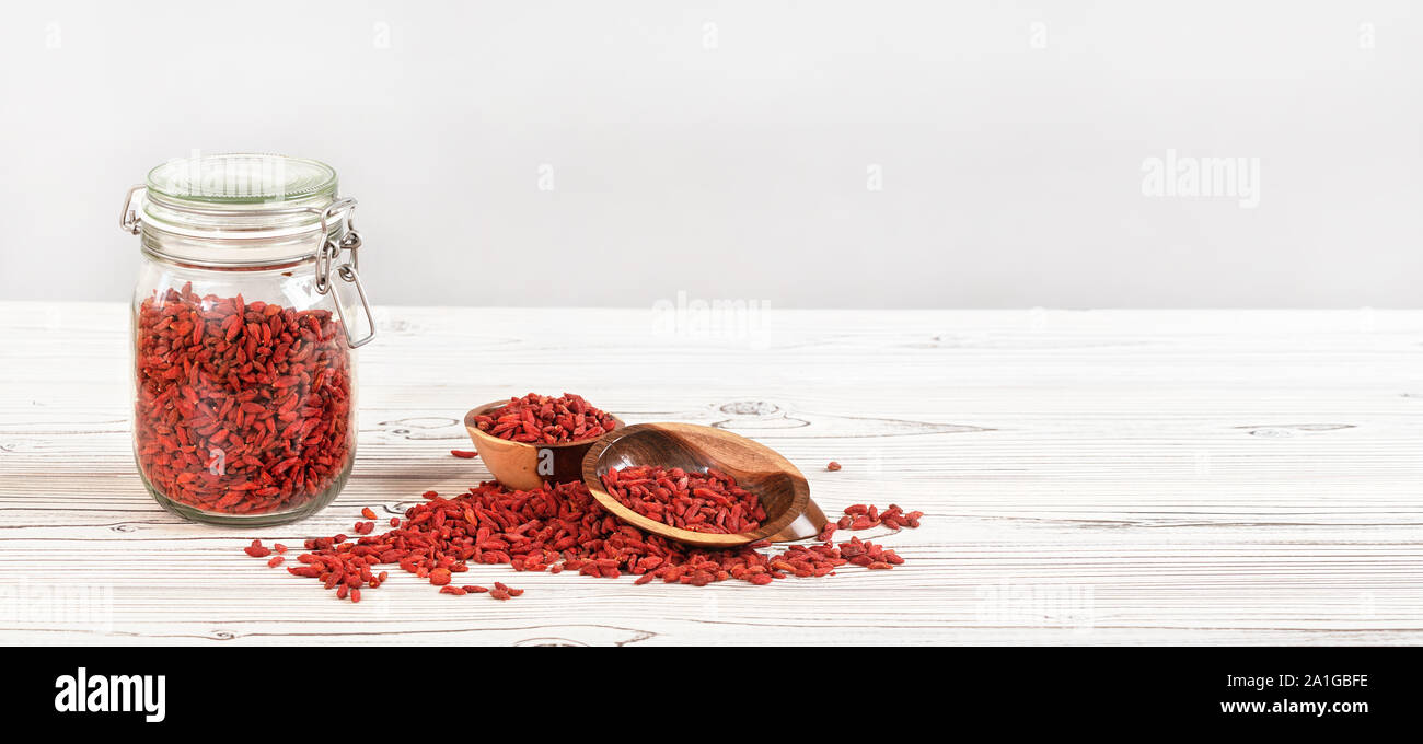 Getrocknete Goji aka. wolfberry in Glas Flasche, einige in hölzernen Schüsseln und auf Whiteboards Schreibtisch verschüttet, Platz für Text auf der rechten Seite Stockfoto