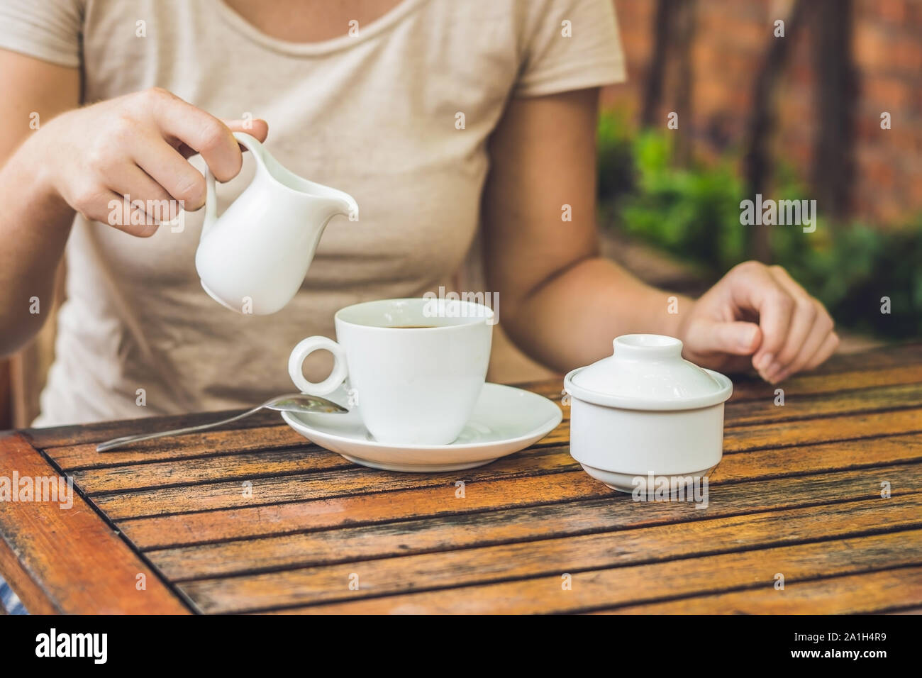 Woman's Hand gießen Milch in weißen Tasse Kaffee im Café im Freien. Stockfoto