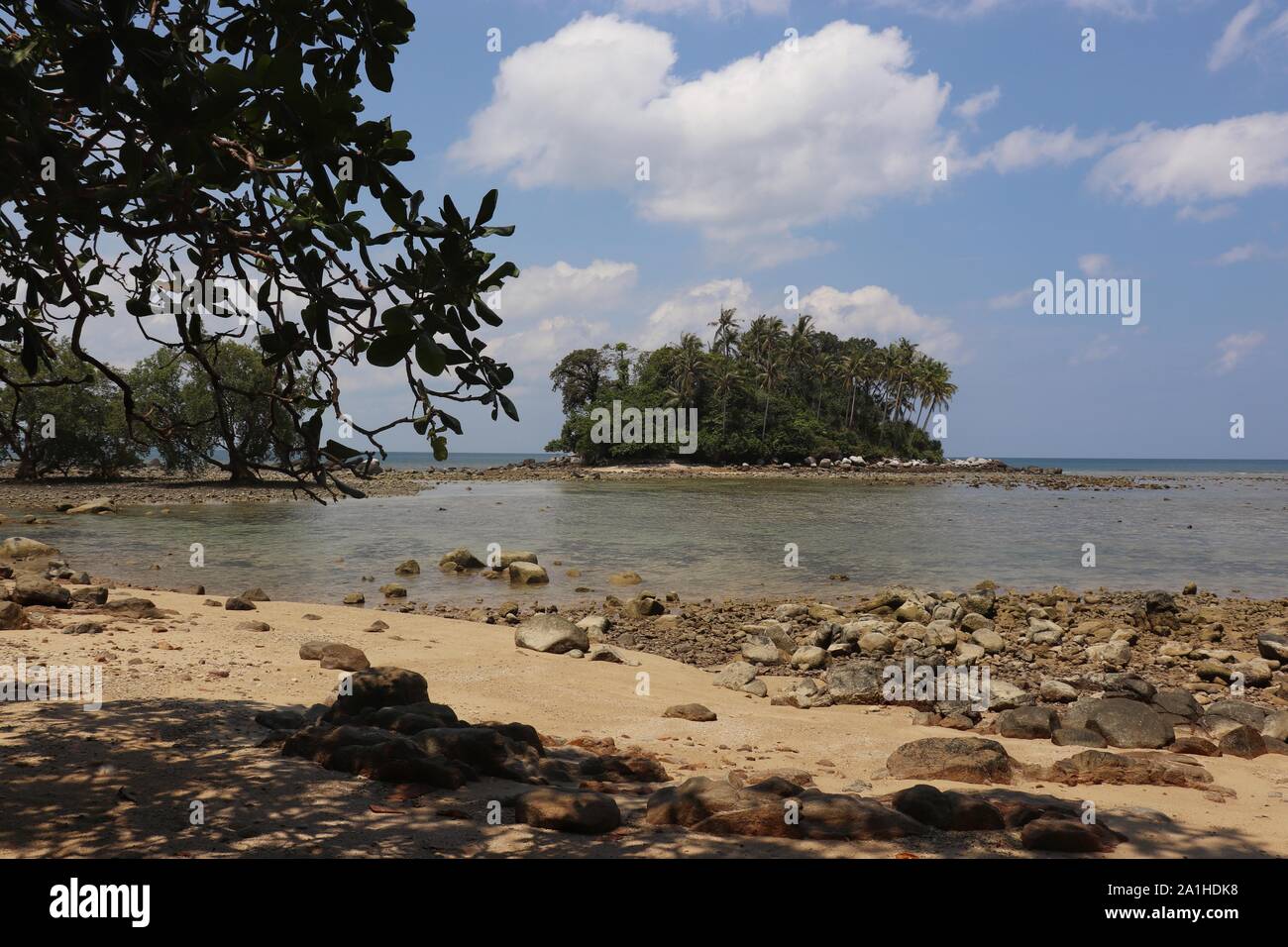 Tropischer Strand mit Sand und Steine, Blick auf das Meer und die grüne Insel durch Blätter, selektive konzentrieren. Konzept der Entspannung im Paradies der Natur Stockfoto