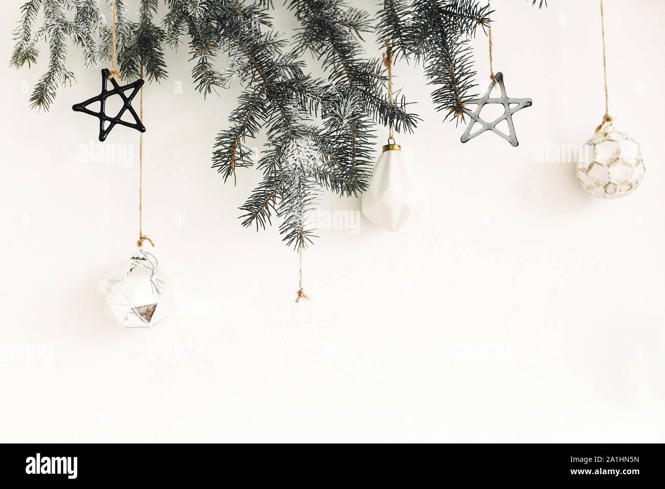 Stilvolle Weihnachten Ornamente auf Tanne Zweig hängend auf der weißen Wand. Kreative Weihnachten festliche Dekoration. Kiefer Zweig mit Vintage Glas Spielzeug. Moderne Zusätzl Stockfoto