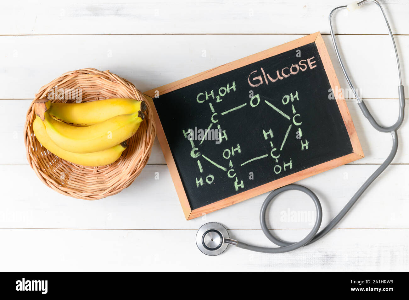 Glukosemolekül auf Tafel mit Banane und Stethoskop auf hölzernen weißen Hintergrund, Ernährung und Lebensmittelkunde Konzept Stockfoto