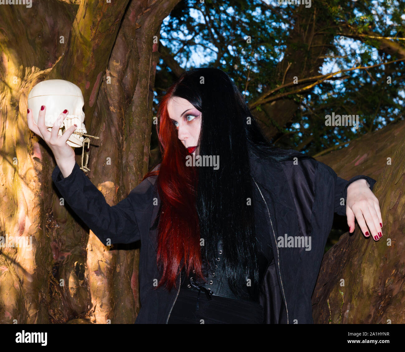 Dunkle und geheimnisvolle junge Frau in Schwarz gothic Kostüm spricht mit menschlichen Schädel in der mittelalterlichen Kirche Friedhof gekleidet Stockfoto