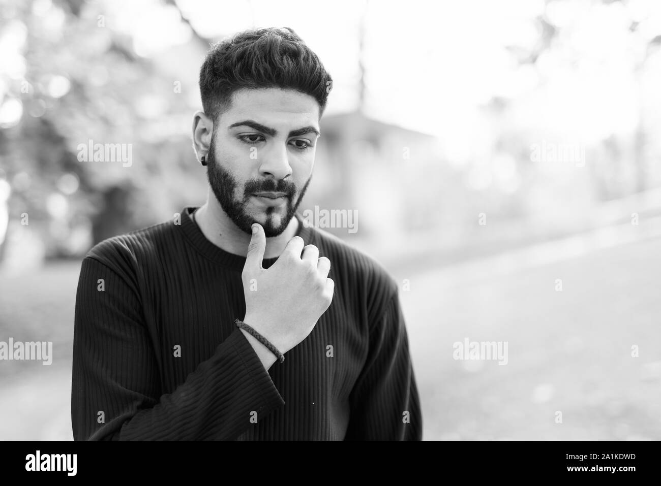 Junge schöne Indische Mann Denken mit der Hand am Kinn im Park Stockfoto