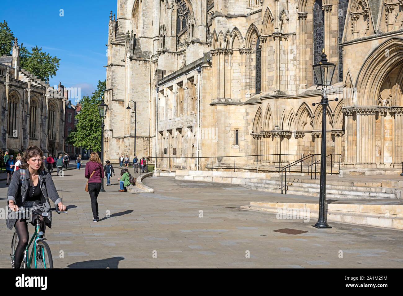 Basis des York Minster Kathedrale und Metropolitan Kirche St. Peter, UK mit Fußgängern in der Straße und die junge Frau auf dem Fahrrad nähert. Stockfoto