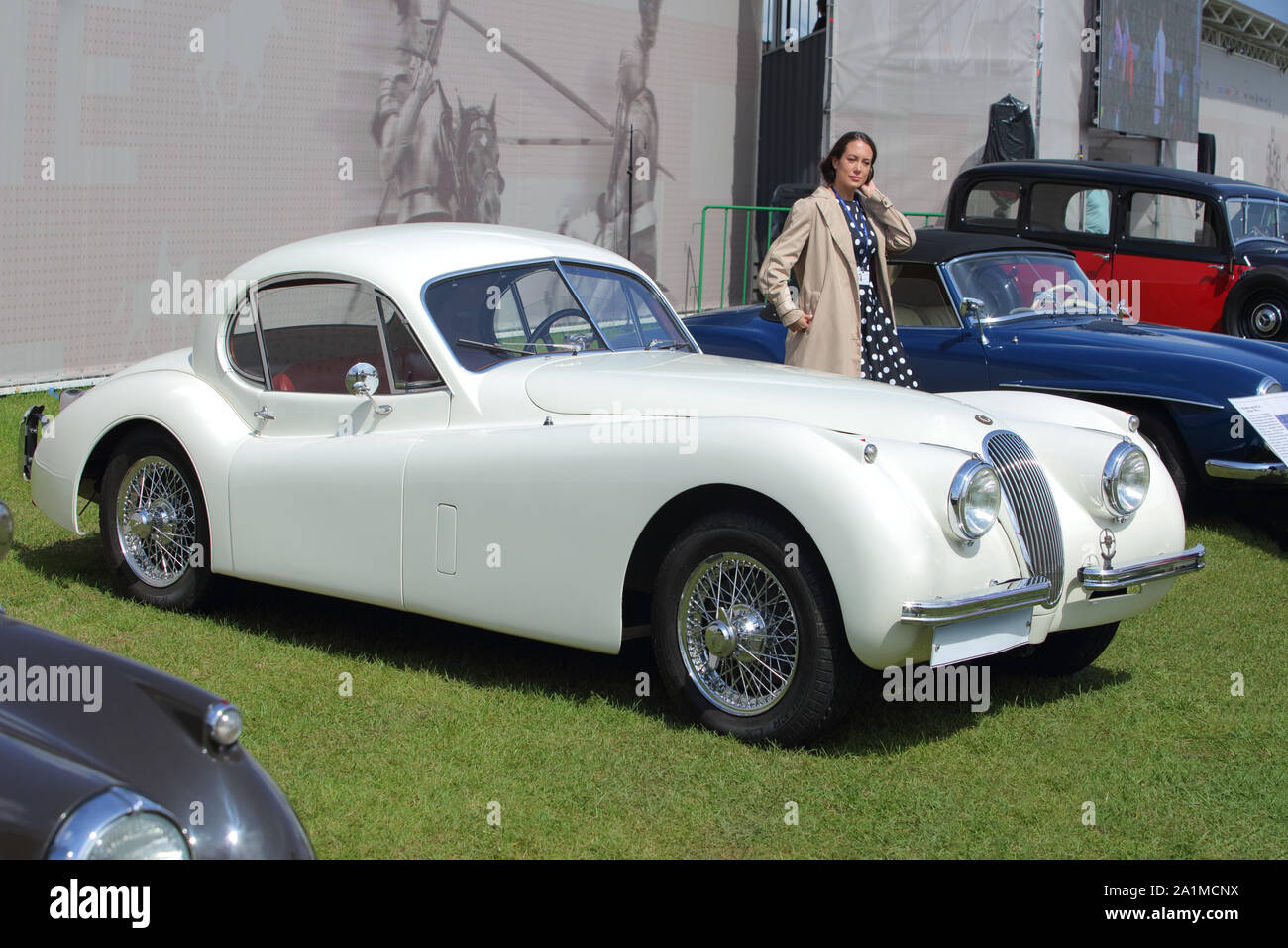 Glamourou Mädchen im Zeitraum Kleid posiert in der Nähe von Jaguar XK 1956 140 MC Coupé Stockfoto