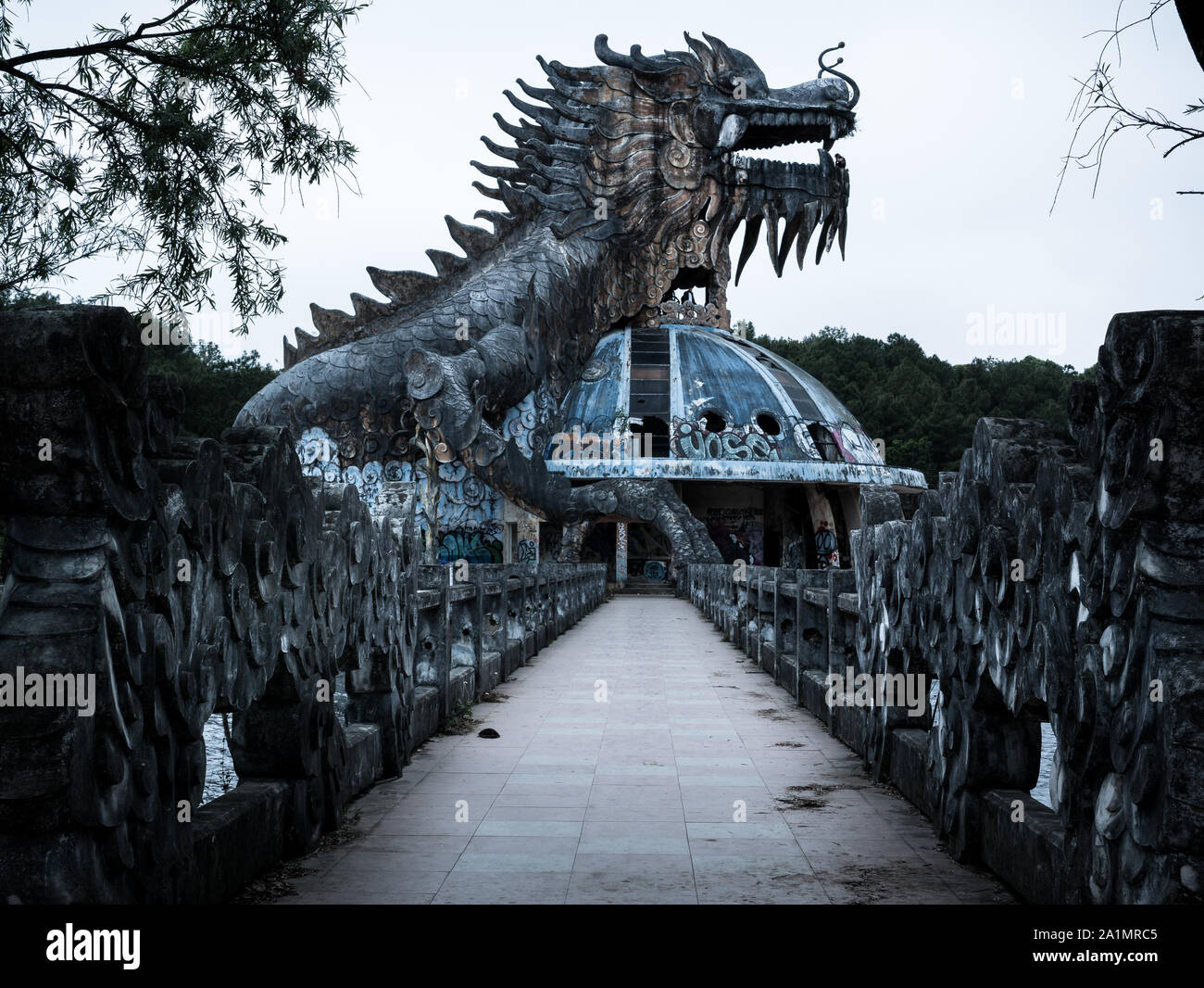 Riesig und unheimlich stone Dragon mit Spikes und offener Mund mit Zähnen in der Seitenansicht mit Fußweg an verlassenen Water Park, Thuy Tien See, Hue, Vietnam Stockfoto