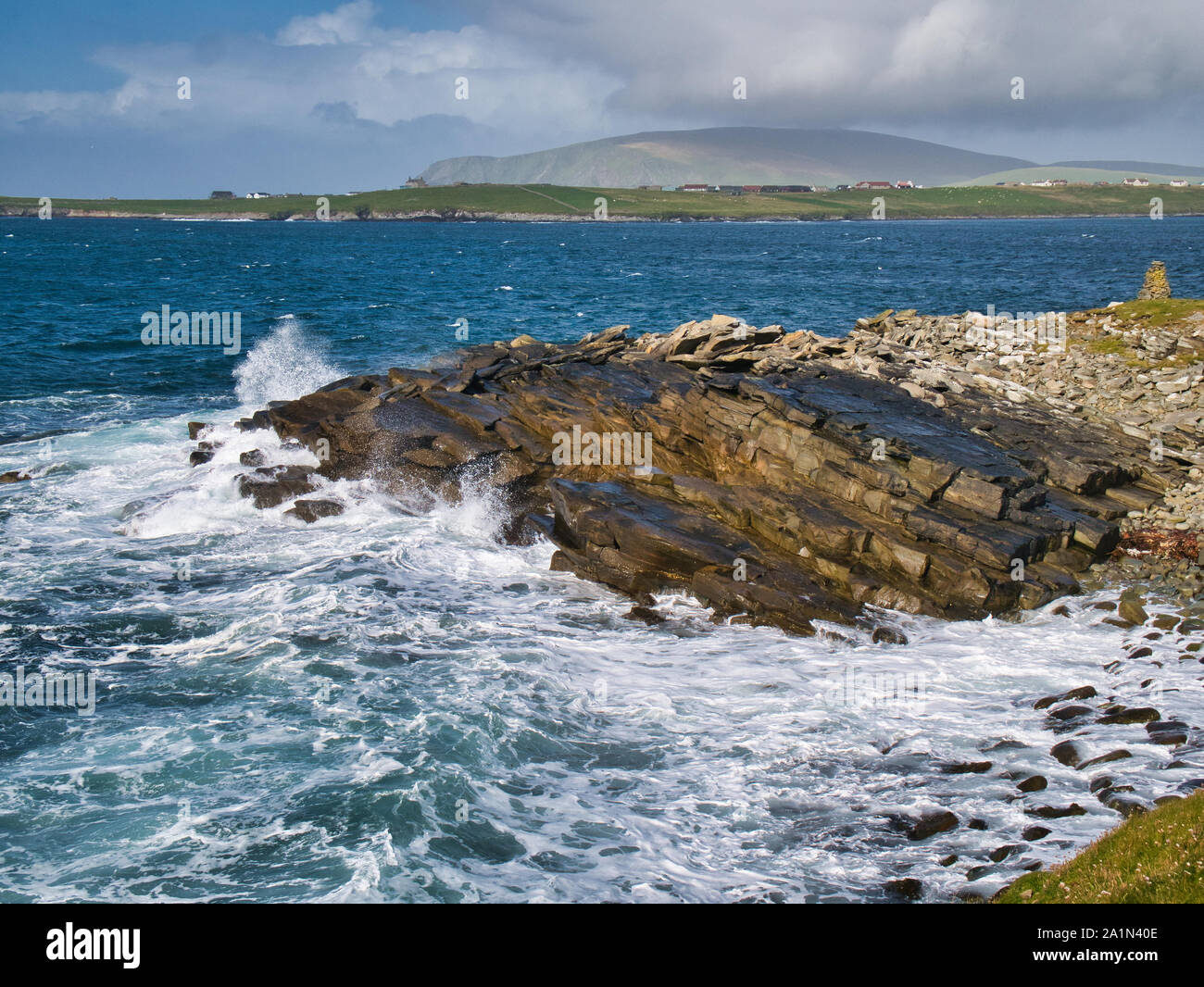 Wellen auf schrägen Sandsteinfelsen auf der South Shetland Küste in der Nähe von Sumburgh Head, Gesteinsschutt fegte durch die Wellen auf der rechten Seite. Der Hügel von F Stockfoto
