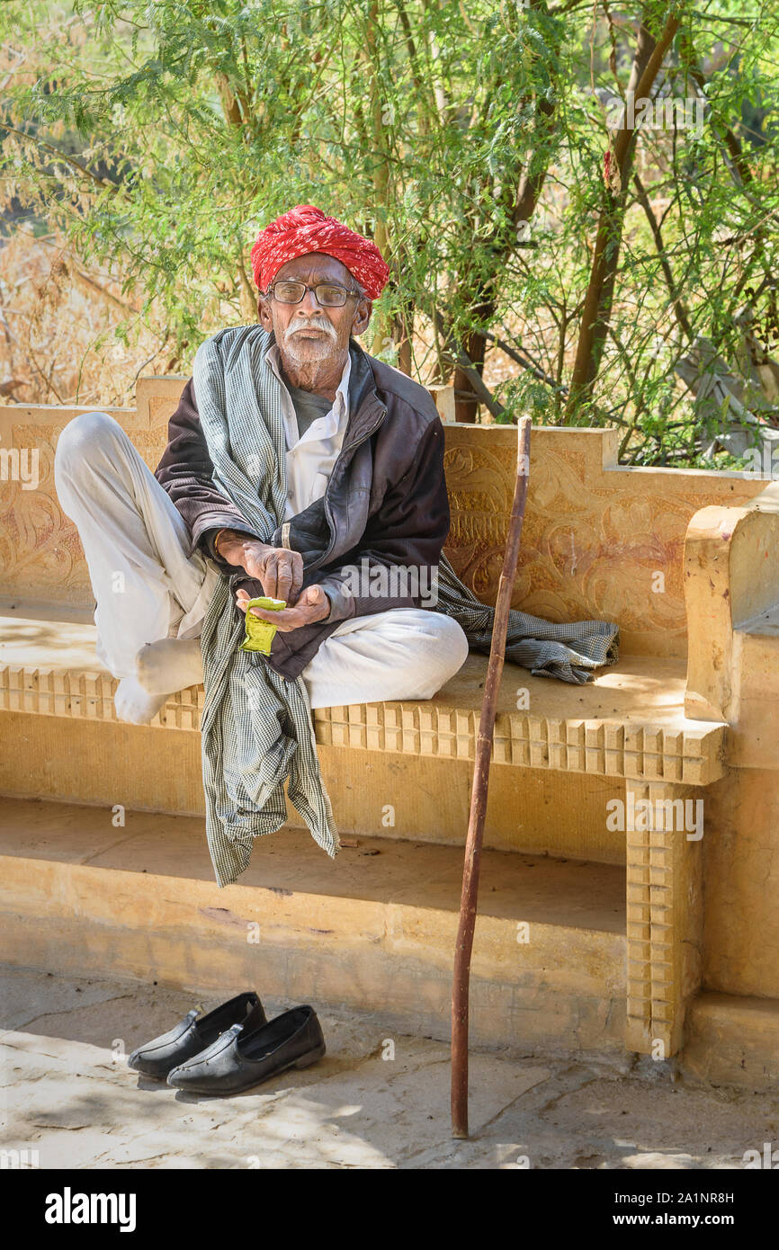 Jaisalmer, Indien - Februar 16, 2019: Ältere indische Mann mit grauen Schnurrbart trägt rote Rajasthani turban oder pagari auf der Bank in Jaisalmer. Rajastha Stockfoto