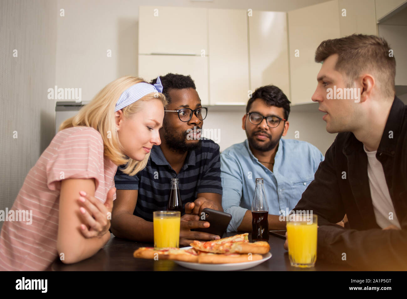 Gruppe von diversen Freunden am Tisch sitzen, essen Pizza, Saft trinken, über Handy, zusammen prüfen neue Telefon-APP. Multikulturellen Studenten ha Stockfoto