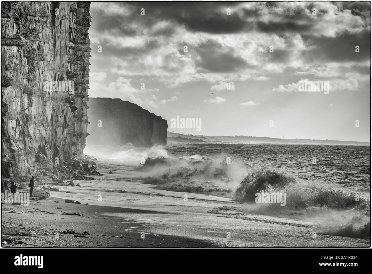 Schwarze und weiße Schuß von zwei Personen, stehen unter einem Felsen beobachten große Wellen werfen. 99/100 x 50 Stockfoto