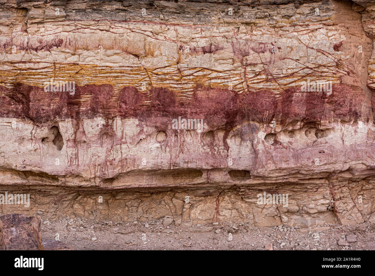 Eine Klippe in der makhtesh Ramon in Israel zeigen verschiedene Schichten von Gesteinen und Böden, darunter eine rote Schicht, Blutungen in der Ebene darunter Stockfoto