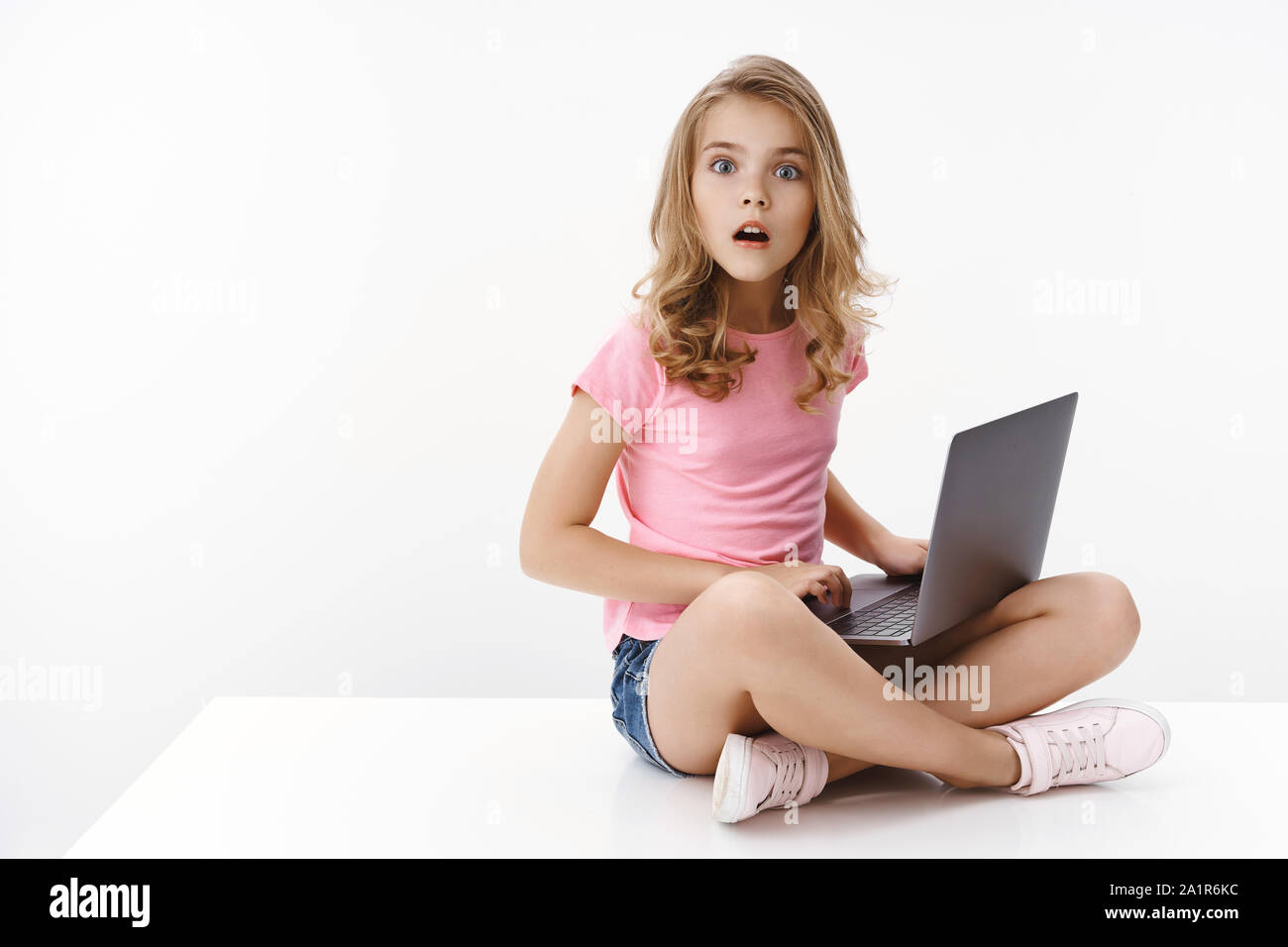 Staunen erregt Smart niedlichen Europäischen kleines Mädchen, sitzen gekreuzten Beinen laptop, Studium online e-learning, abwenden, pc-Bildschirm starren Kamera begeistert Stockfoto