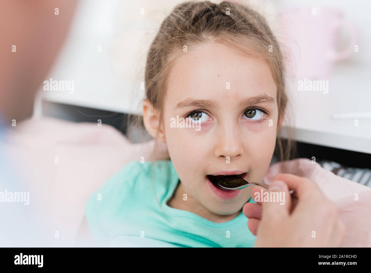 Kranken kleinen Mädchen ihren Mund öffnen und die Medizin von Spoon von Arzt gehalten, während ihm Stockfoto