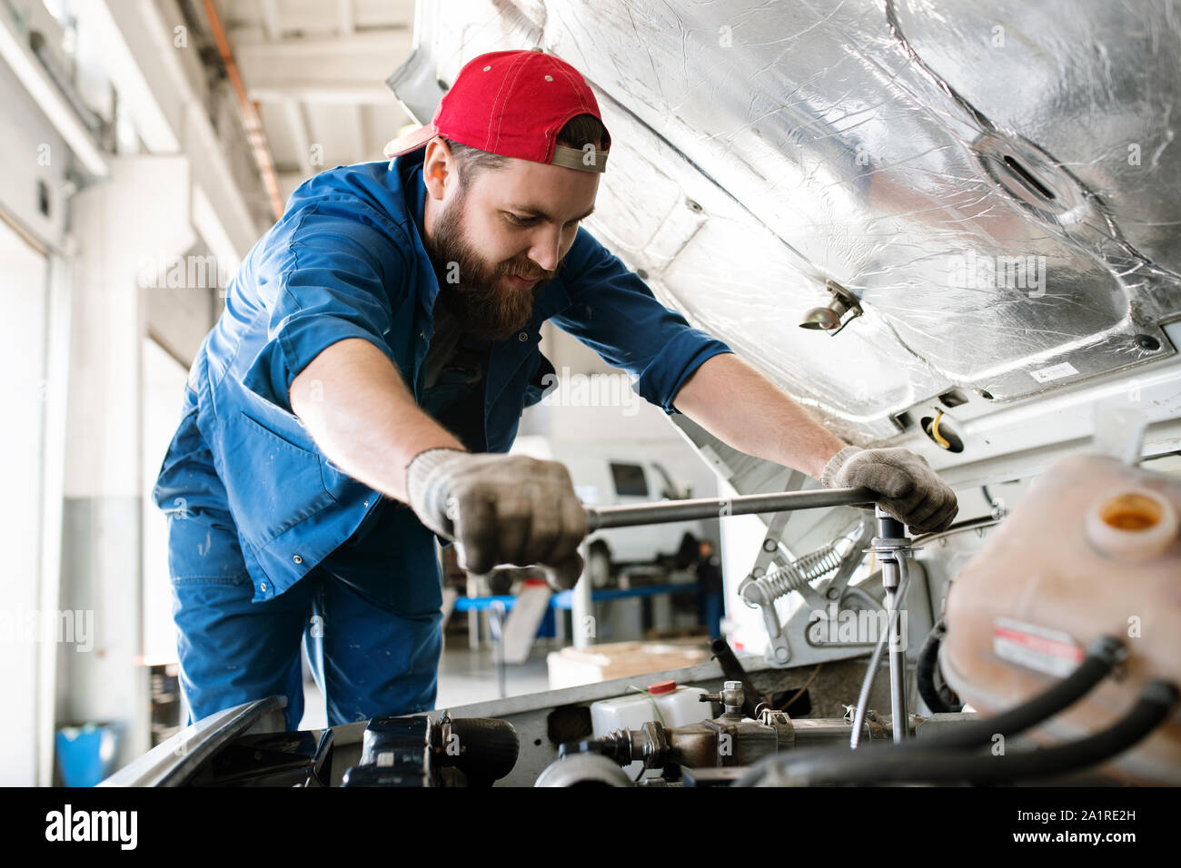 Junge Techniker in Arbeitskleidung biegen über Motor des Pkw oder Lkw bei der Prüfung oder für die Behebung von kleinen Details Stockfoto