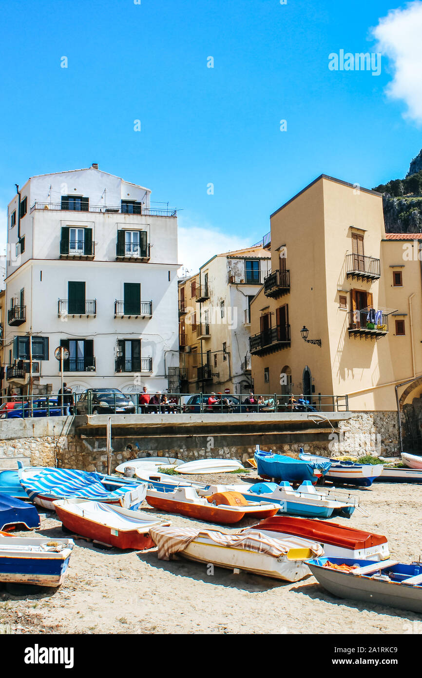 Cefalu, Sizilien, Italien - Apr 7, 2019: Schöne alte Hafen der kleinen sizilianischen Dorf. Fischerboote am Strand. Traditionelle Häuser, die Berge im Hintergrund. Die Menschen auf der Promenade. Stockfoto