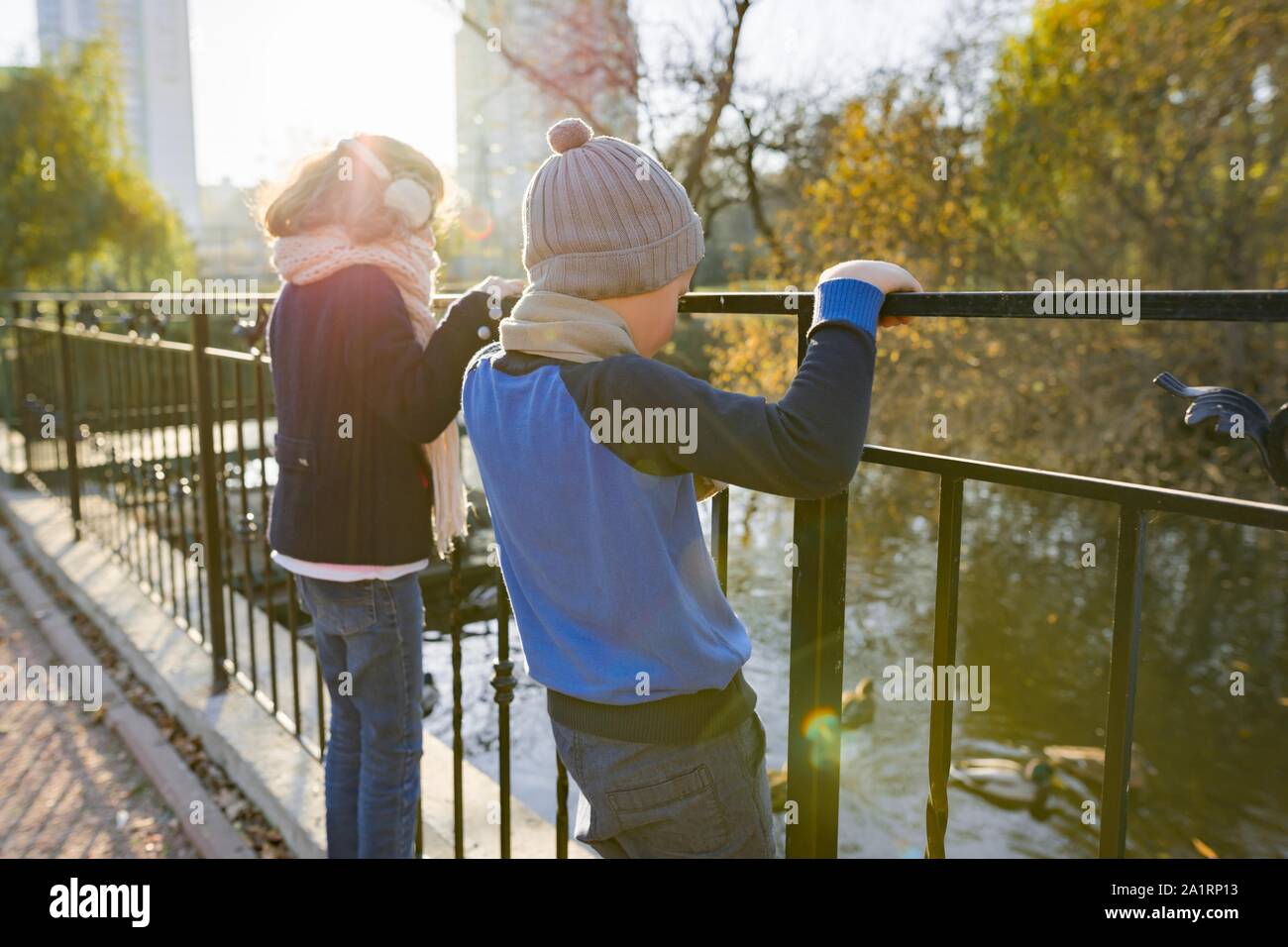 Kinder, Junge und Mädchen stehend rücken Brücke, an Enten, sonnigen Herbsttag im Park suchen, goldenen Stunde Stockfoto