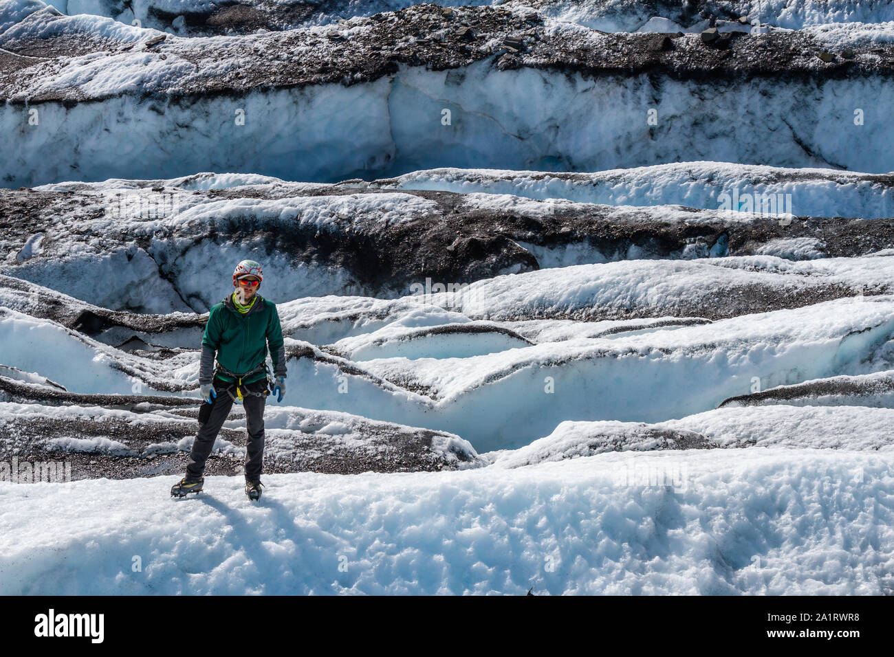 In einem Feld von Gletscherspalten, ein Mann steht auf einer Rippe des weißes Eis. Hinter ihm sind Reihen von gebrochenem Eis in Moräne abgedeckt - Schmutz und Rock. Stockfoto