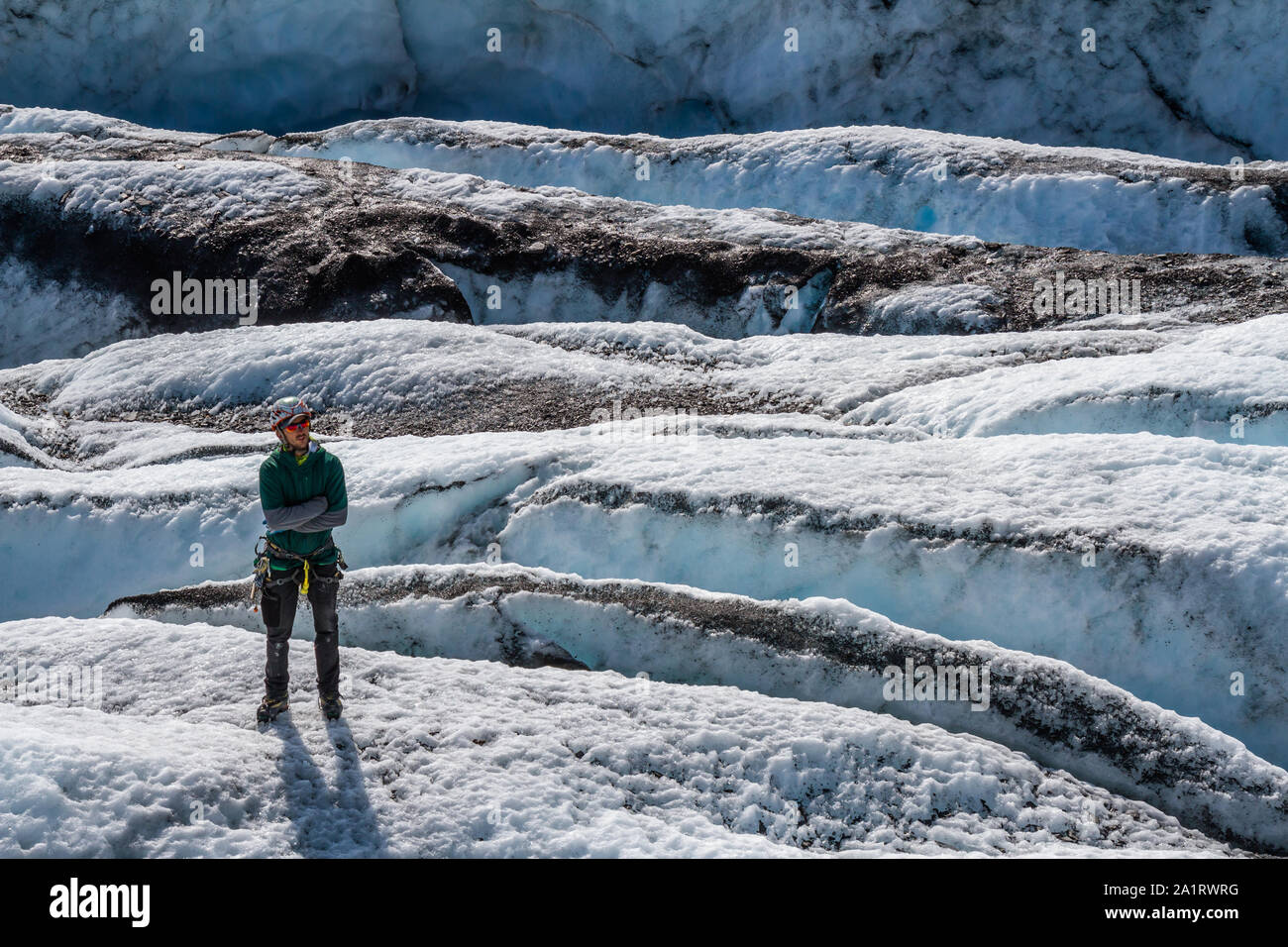 Unter gebrochenem Eis zwischen vielen Gletscherspalten, ein Führer in einer grünen Jacke steht stoisch mit verschränkten Armen. Stockfoto