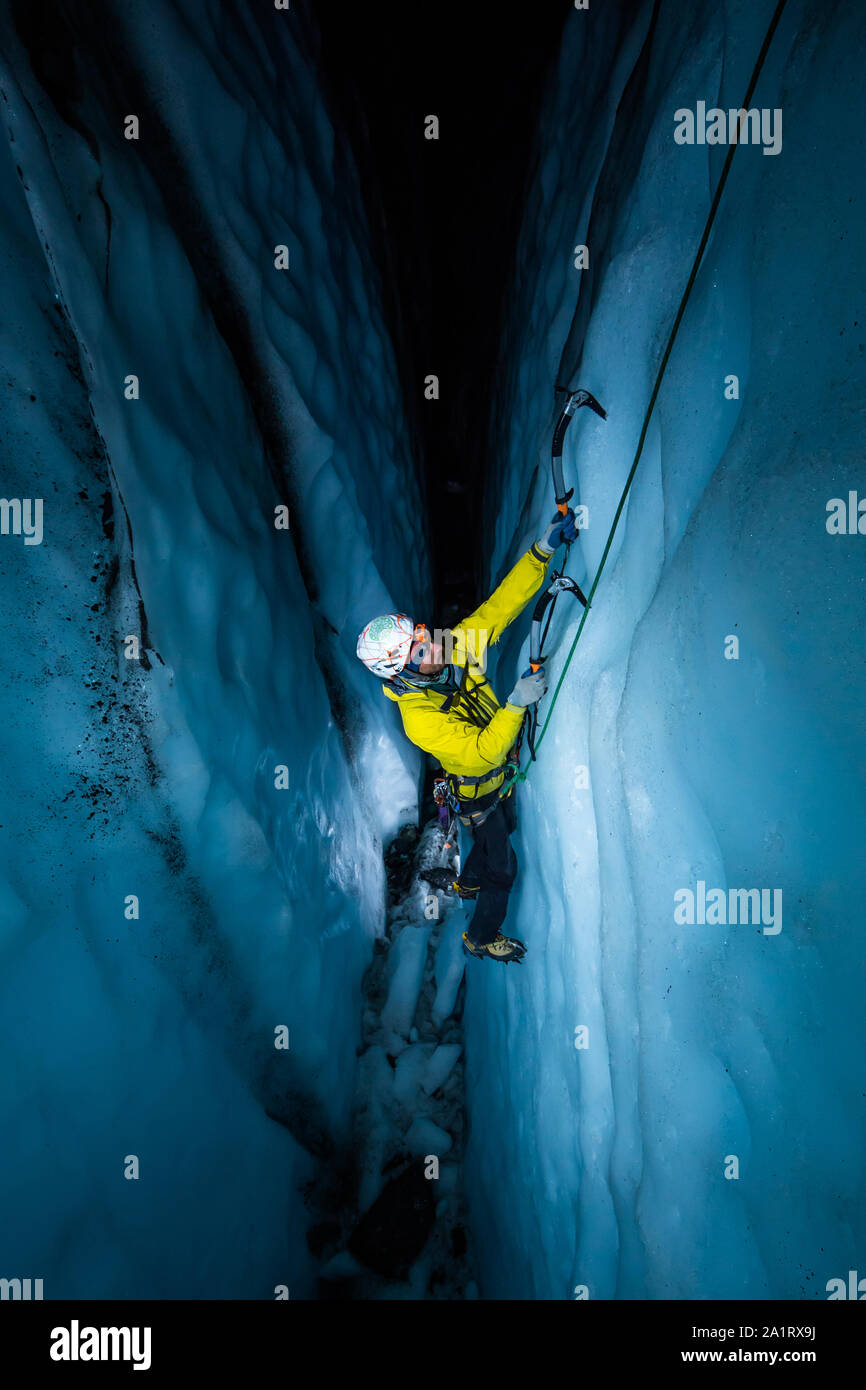 Athlet Eisklettern in eine Gletscherspalte in der Nacht durch künstliches Licht beleuchtet, wie Er klettert aus dem dunklen Gletscherspalte. Stockfoto